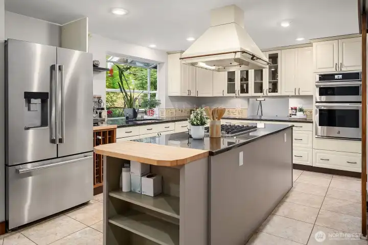 The chef's kitchen is beautifully appointed with granite and slate counters, generous cabinetry, high-end appliances, and a charming butcher block island, all overlooking the deck and lush greenbelt beyond.