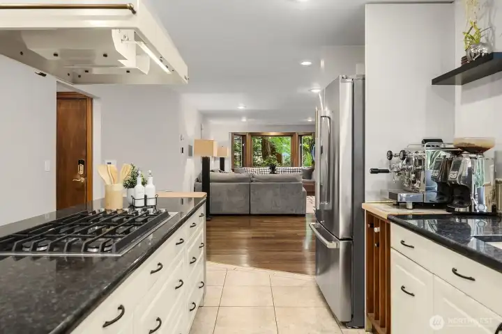 Another angle of the well-appointed kitchen highlights the dark slate counters, quality appliances, and excellent storage, all flowing naturally toward the dining and living spaces beyond.