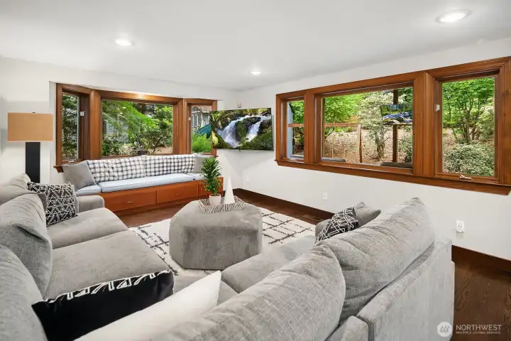 The warm and inviting family room features a full wall of windows that frame the serene greenbelt, flooding the space with natural light and bringing the beauty of the outdoors in.