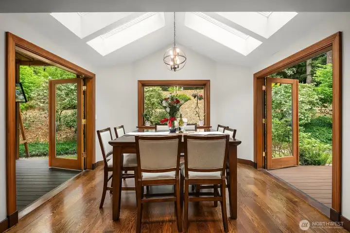 Another angle of the dining space highlights the soaring skylit ceiling, warm wood tones, and seamless connection to the kitchen and outdoor living areas beyond.