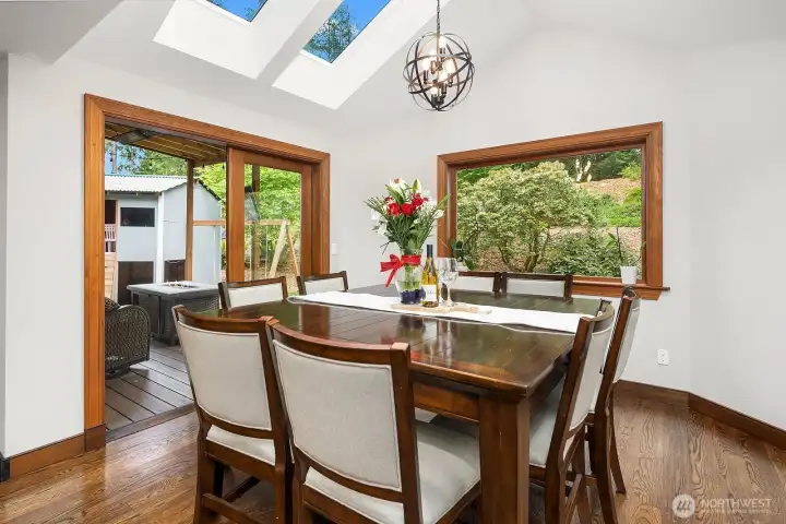 The bright dining area is bathed in natural light from a skylight overhead and surrounded by windows with views of the lush landscaping, creating a beautiful setting for everyday meals and special gatherings alike.