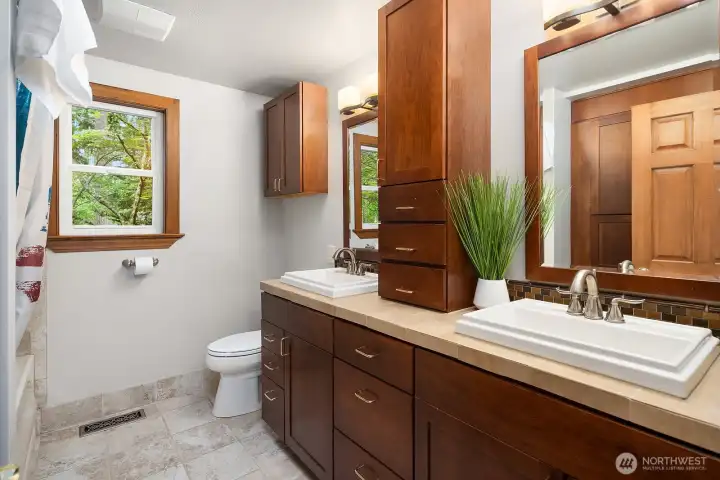 The guest ensuite bath features warm wood cabinetry, a tiled shower, and a bright window, offering a private and beautifully finished space for guests.