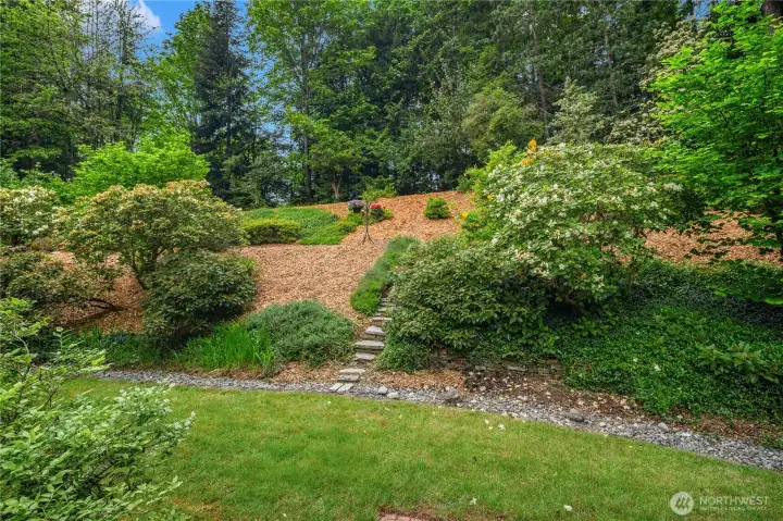 The beautifully terraced landscaping features lush gardens, mature plantings, and a meandering path that winds through the serene greenbelt setting, creating a truly parklike atmosphere right in your own backyard.