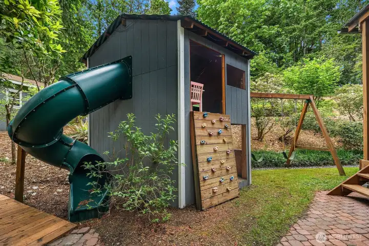 The charming kids play fort with slide is tucked among the mature trees, offering a magical outdoor play space that makes this backyard truly one of a kind.