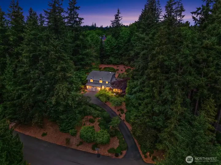 This breathtaking dusk aerial reveals the home's magical setting, with warm lights glowing through the trees and the beautifully landscaped grounds creating an enchanting and deeply private retreat.