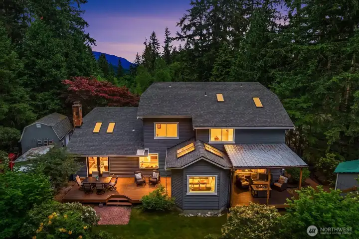 This stunning twilight aerial captures the home glowing warmly against the lush evening landscape, perfectly showcasing the exceptional architecture, expansive deck, and magical setting that make this property truly one of a kind.