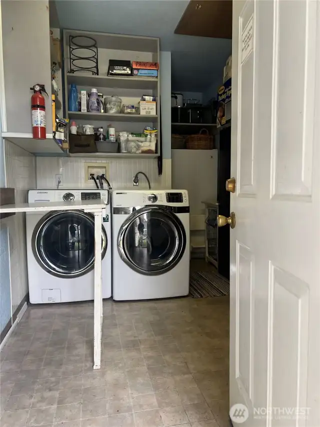Laundry area off the kitchen doubles as a pantry/storage  area and houses a freezer plus washer/dryer and folding table. Note attic access on the ceiling.