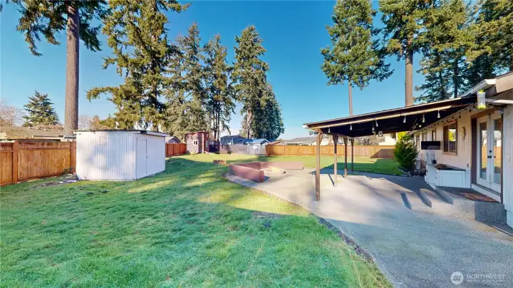 Fully fenced backyard offering a covered patio, firepit area, garden shed, and a playhouse.