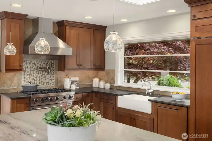 A kitchen built for serious cooking—anchored by a Viking 6-burner gas range, Viking hood, and pot filler, with a porcelain farmhouse sink set beneath natural light. Grohe fixtures, quartz countertops, and warm shaker cabinetry elevate every detail.