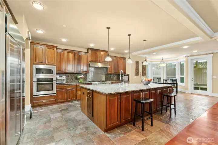 Chef’s kitchen featuring a Jen air 6-burner range with griddle, built-in GE Monogram refrigerator, wall oven and microwave, two Bosch dishwashers, beverage refrigerator, pot filler, and a built-in desk area.