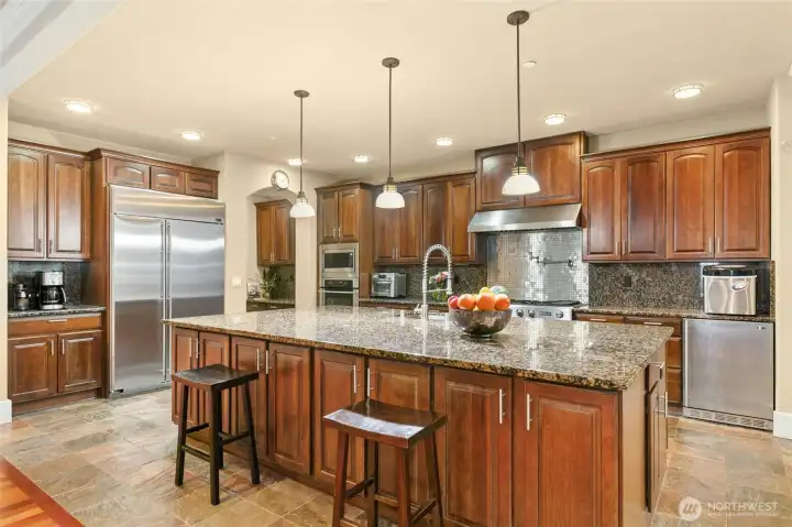 Chef’s kitchen featuring a Jen air 6-burner range with griddle, built-in GE Monogram refrigerator, wall oven and microwave, two Bosch dishwashers, beverage refrigerator, pot filler, and a built-in desk area.