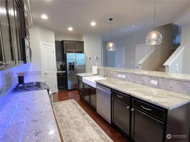 Close-up of the Quartz Counters with reflections of Under-Cabinet-Lighting, Under-counter Farm Sink, Pantry Door and Stainless Steel Appliances.