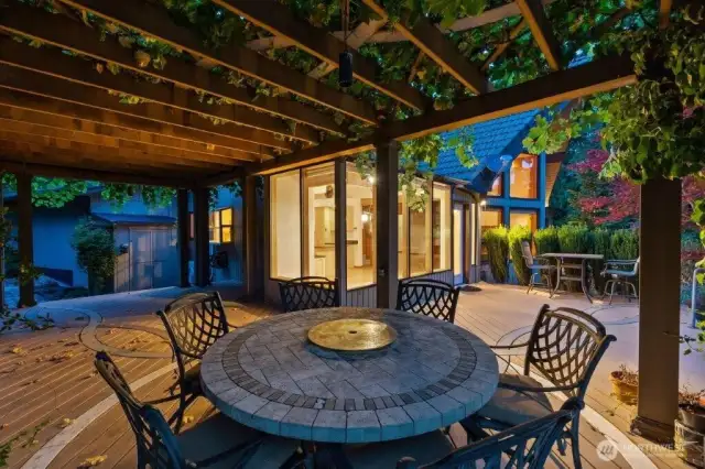 The vine-draped pergola creates a sheltered outdoor dining area on the deck.
