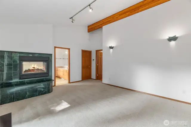 Primary bedroom with cathedral ceilings, french doors to a deck area on the water side of the home, large primary bathroom with propane fireplace, and a custom walk in closet.