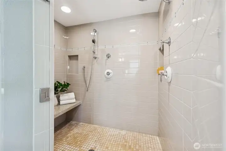Huge walk in shower has shower bench, tile floor and walls, multiple shower heads and tiled shower niche.