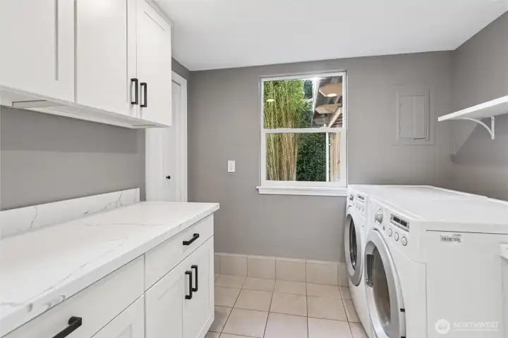 Utility room has tile floor, vanity with deep sink and shelf above the included washer and dryer.  Opposite side has wall and base cabinets with quartz countertop and backsplash.  Washer and dryer are included. Storage closet with shelves too.