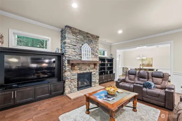 Open living room features grandiose stone fireplace, dark built-in, mirroring windows and recessing lighting.