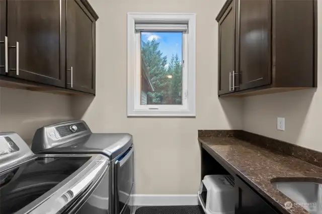 Spacious laundry room offering abundant cabinet storage, sink, and a window that fills the space with natural light, making chores a breeze.