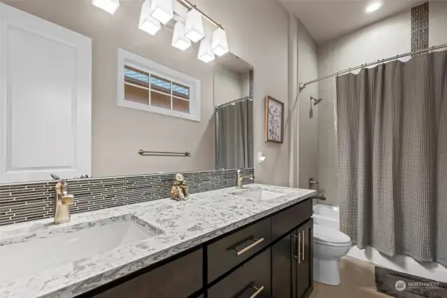 The main downstairs bathroom features dual sinks on quartz counters and beautifully detailed tiling, combining functionality with sophisticated design.