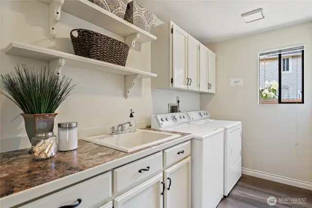 Main floor laundry room with built-in cabinets, sink, shelving, and washer and dryer included.