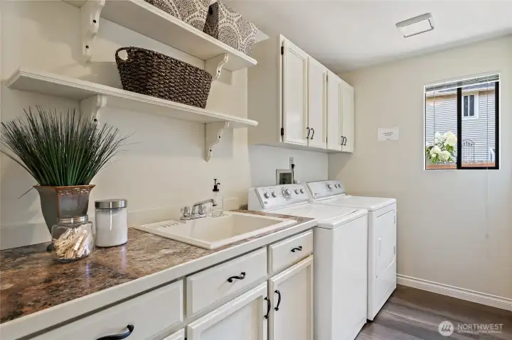 Main floor laundry room with built-in cabinets, sink, shelving, and washer and dryer included.