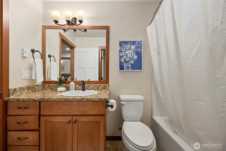 Guest bath with a tub, granite counters, and beautiful wood cabinetry.