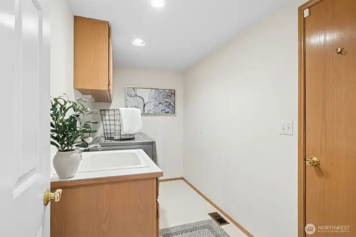 Utility room with a sink and cabinets and a door leading out to the large 3-car garage.