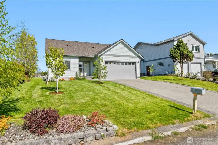 Front exterior with attached two-car garage, driveway parking, and landscaped yard with fruit trees