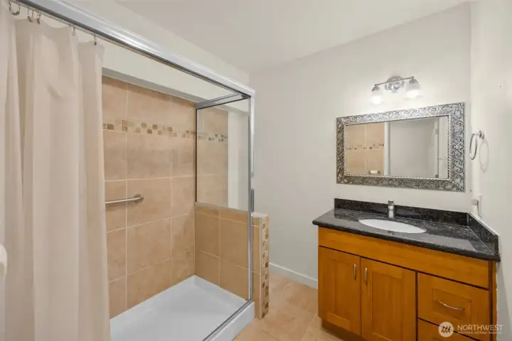 Generous bathroom with a tiled step-in shower, ADA grab bars, and a dark granite vanity.