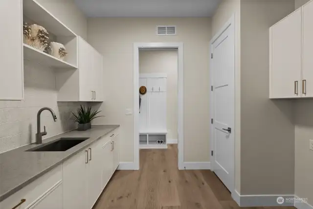 The entrance of the 3-car garage opens into a mudroom, perfect for organizing daily essentials. Continuing beyond, you'll find an expansive laundry room featuring generous counter space for folding laundry and ample cabinetry for storage.