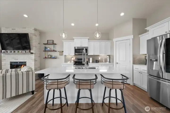 Bright upper-level kitchen featuring quartz countertops, quality cabinetry, stainless appliances, and generous gathering space around the oversized island.