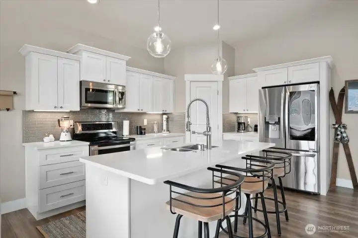 Layered lighting, clean finishes, and oversized island seating give the kitchen a warm and inviting atmosphere.