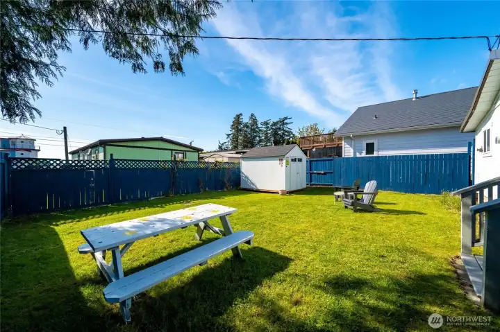 Fully fenced backyard with lush green lawn, cozy seating area, and a versatile storage shed—ready for summer gatherings, gardening, or pets at play.