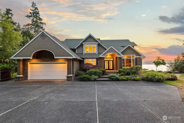 The front facade of the Whidbey Island estate showcases exceptional architectural design harmoniously blending with its natural surroundings. The grand entrance is highlighted by dramatic gabled rooflines and expansive windows that invite abundant natural light.