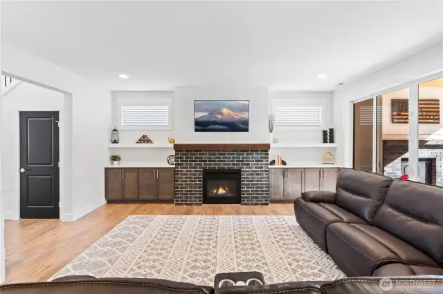 Living room showcases brick-framed gas fireplace and custom built in cabinetry.