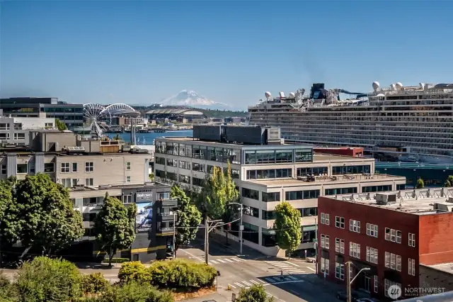 Iconic Seattle, Mt. Rainier rises behind a lively scene of docked cruise ships, the Aquarium, Ferris Wheel, and the buzz of the reimagined Seattle Waterfront.