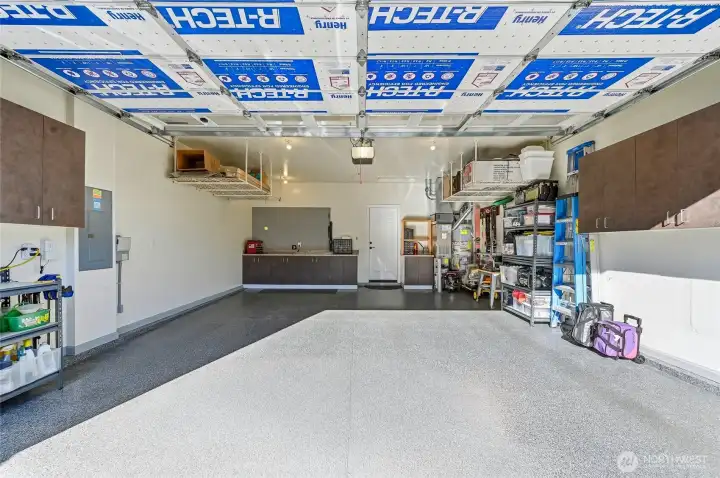 Fully finished garage with new door opener and keypad, epoxy floor, work bench, storage racks and cabinets.