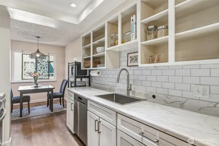 Nicely updated kitchen with a tile backsplash, deep stainless steel sink, newer appliances, updated lighting, and both open and closed shelving.