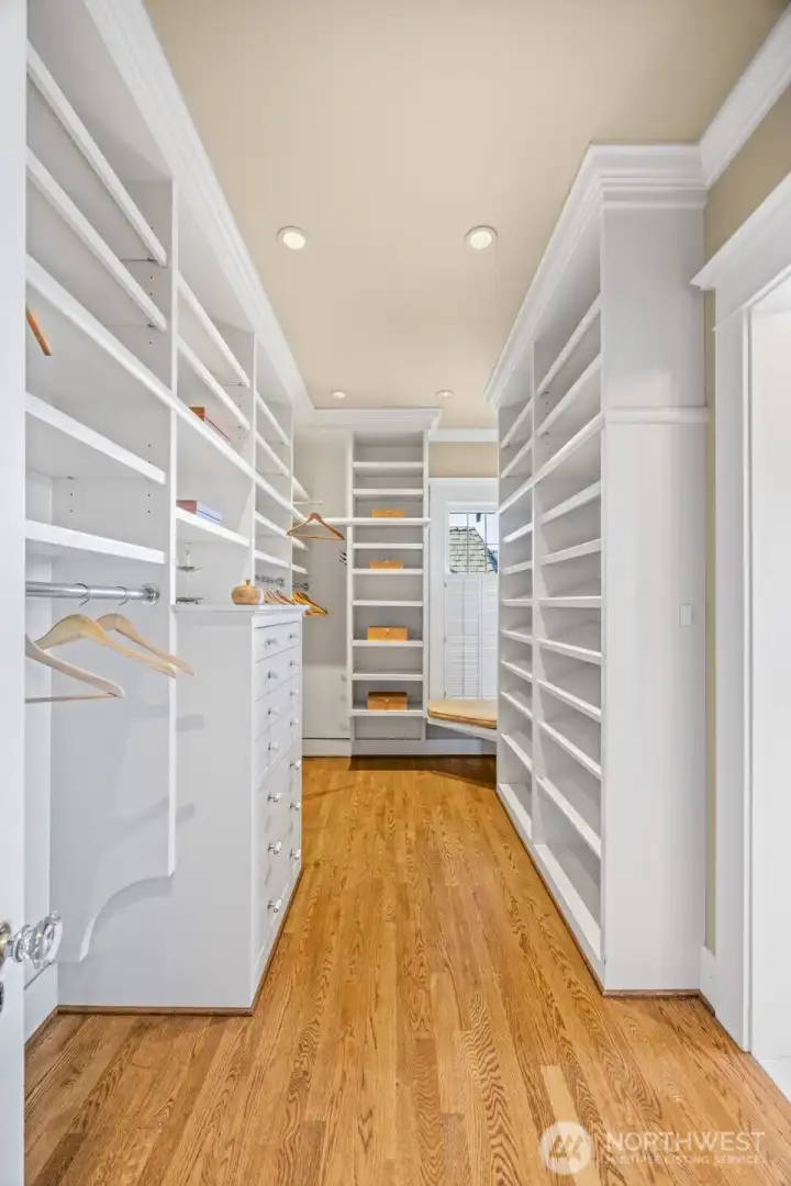A beautifully tailored boutique closet features extensive custom built-ins and a quiet window seat.