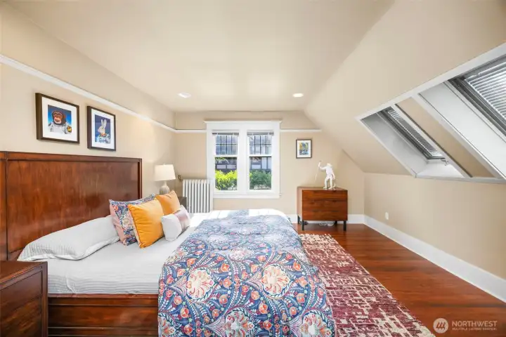 Nestled under architectural rooflines, this sunlit upper bedroom features charming skylights and cozy warmth.