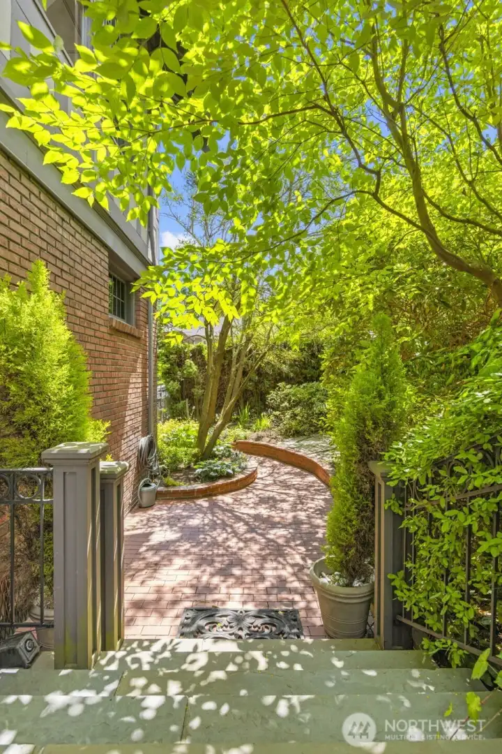 Dappled sunlight warms a winding brick pathway that meanders through beautifully curated garden beds.