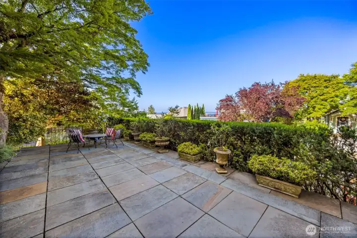 A spacious, stone-paved patio offers a tranquil venue for outdoor lounging beneath a canopy of mature trees.
