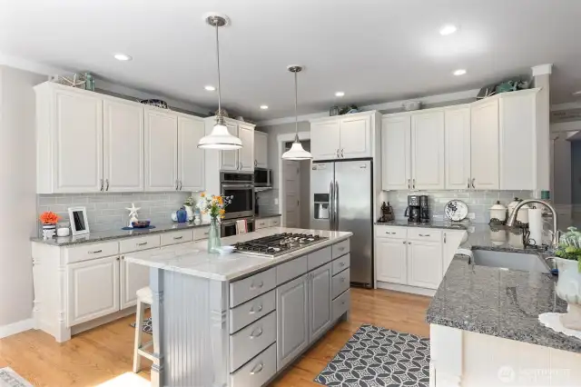Tastefully updated kitchen with natural stone countertops, SS appliances including double ovens, tile backsplash, and soft close and undercabinet lighting.