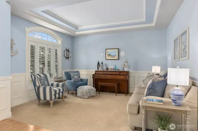Beautifully appointed formal living room with tray ceiling, crown molding, wainscoting and custom plantation shutters.