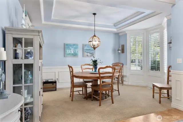 Formal dining room with same tray ceiling and wainscoting detail, crown molding and bay window with custom plantation shutters.