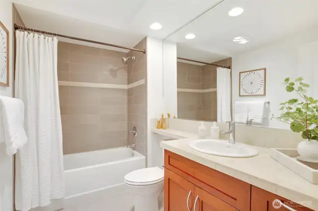 Stone countertop, tile flooring, warm wood cabinetry, and a designer sink complete the full-size bathroom.