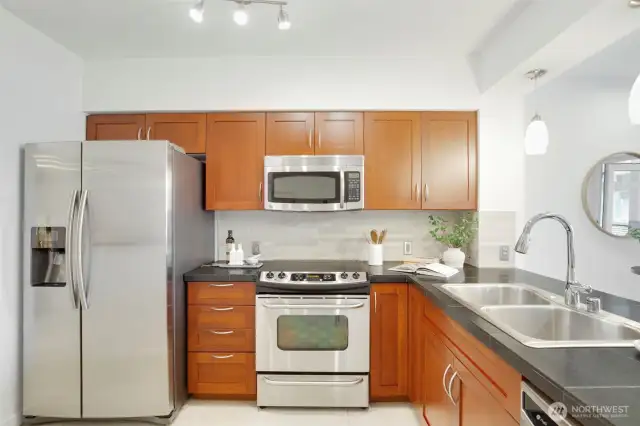 The full-size kitchen features a stainless steel appliance suite, black quartz counters, and cherry cabinets.