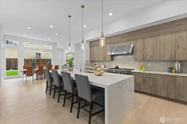 A beautifully composed culinary space where the oversized island, warm wood tones, and effortless flow to the dining area create a kitchen that is as inviting as it is sophisticated.