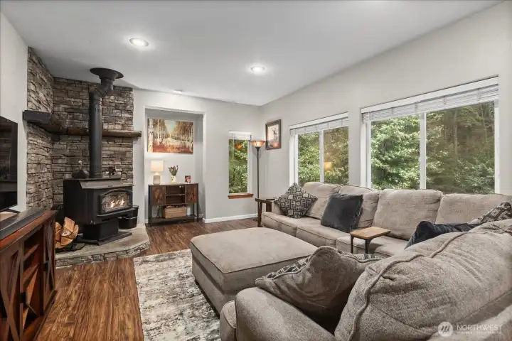 Anchored by a striking stone hearth, the wood-burning stove creates a warm and inviting atmosphere, while expansive windows frame peaceful views of the surrounding greenery.