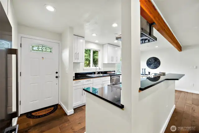 A welcoming entry with modern touches—Upgraded kitchen with white cabinetry, granite counters, and stainless appliances, the kitchen opens to a warm and inviting living space anchored by engineered hardwoods and a striking wood-accent beam.